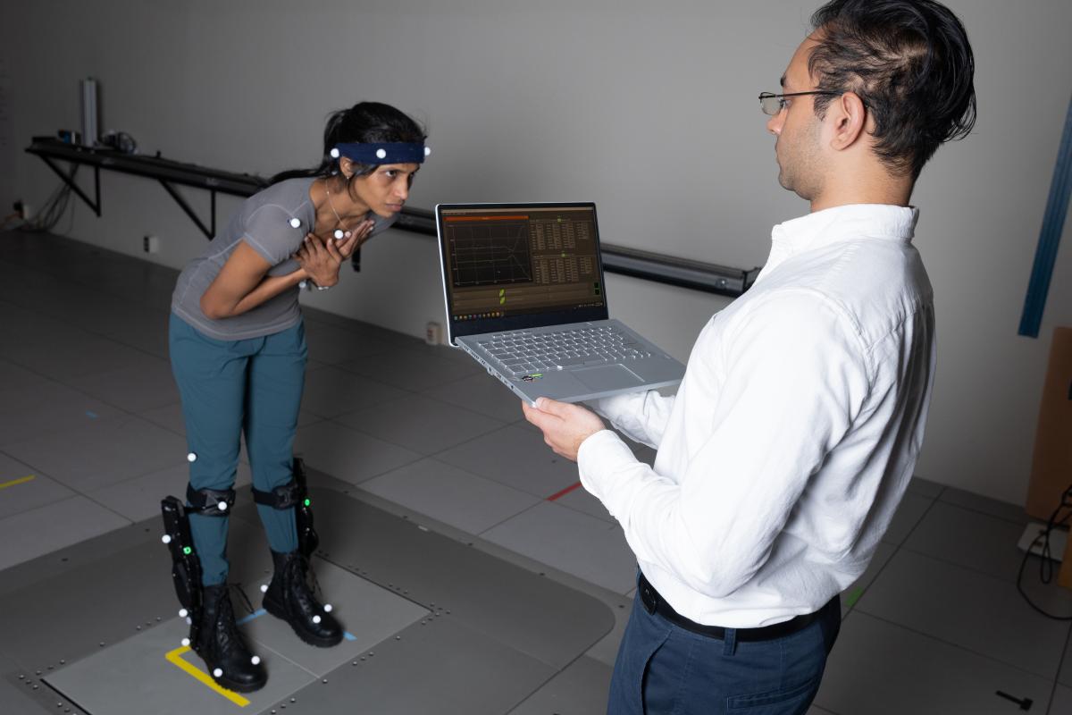 Postdoctoral fellow Surabhi Simha demonstrates how researchers tested whether robotic ankle exoskeleton boots can help people with their balance when its disrupted. Subjects wore sensors for motion capture, muscle activity, and ultrasound while they stood on a platform that shifts abruptly to disrupt their balance. Research engineer Rish Rastogi, right, monitors some of the data being collected. 