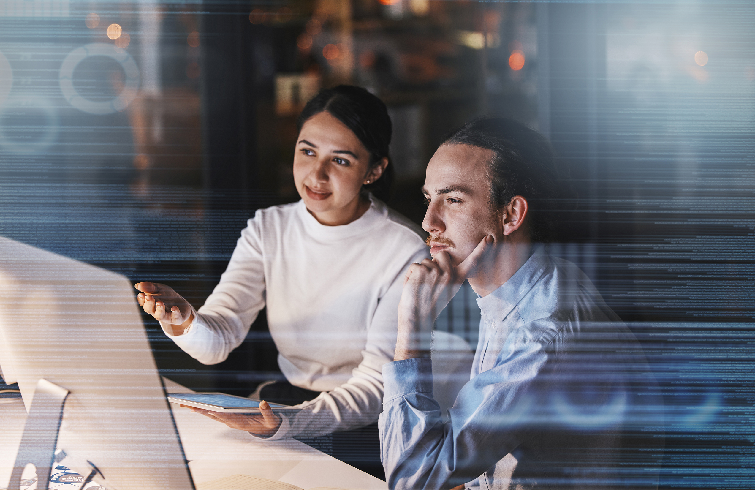 A woman and a man working at a desk sitting in front of a computer monitor.
