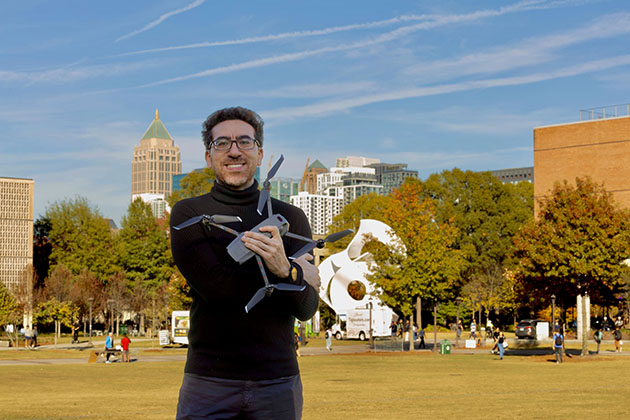 Male researcher standing on the Georgia Tech campus while holding a drone in his arms.