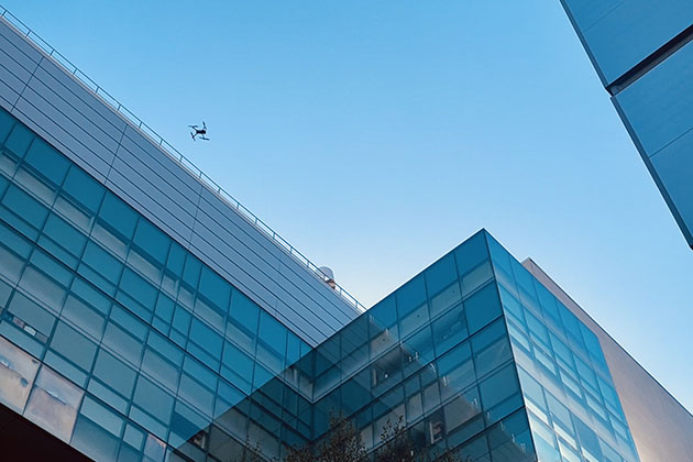 A drone flying high between several buildings with the sky in balcground.