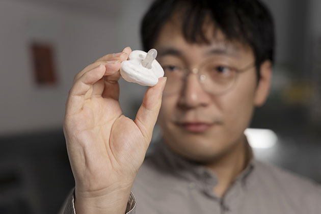 Male researcher in background holds a pacifier up close in foreground