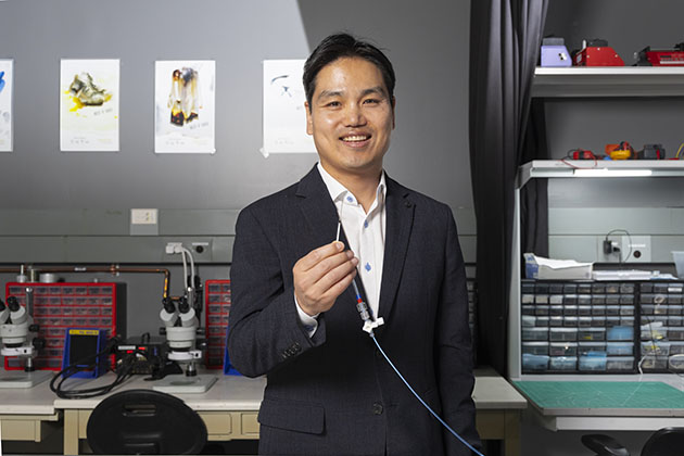Male researcher wearing a black suit holds a small sensor while standing in a lab at Georgia Tech.