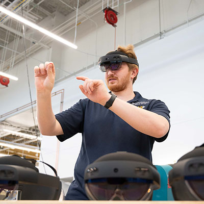 male student speaking in fron of a classroom while wearing augmented reality goggles