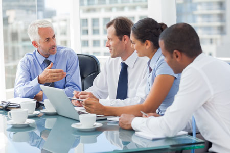 Several people sitting at a conference table with a laptop, meant to illustrate the collaborative nature of technology transfer.