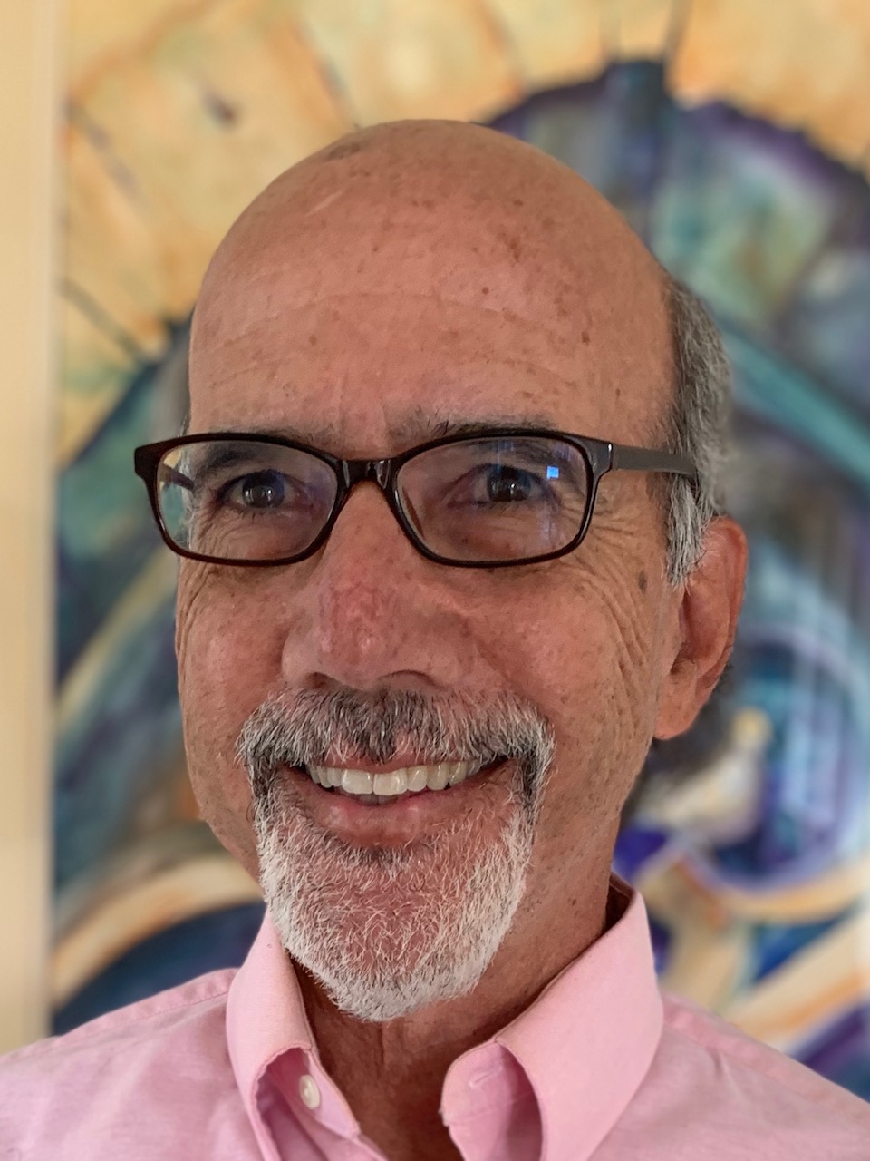 A man with glasses, a goatee, and a pink collared shirt 