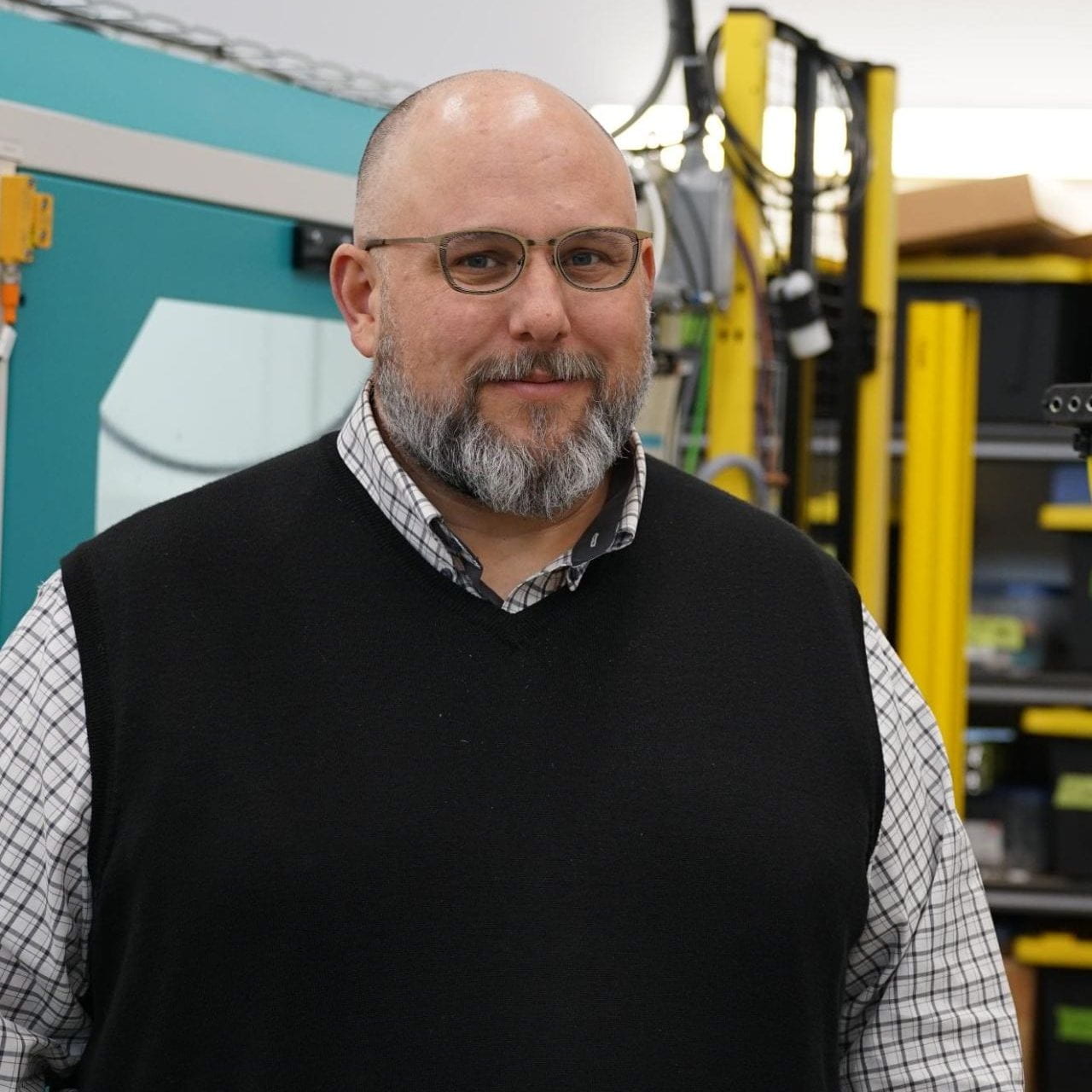 A man with glasses and a beard in a dark vest and dress shirt