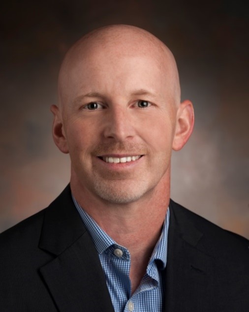 A headshot of a man in a blue shirt and dark blazer