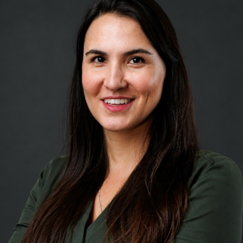A woman with long dark hair wearing a dark green blouse smiles for a portrait.