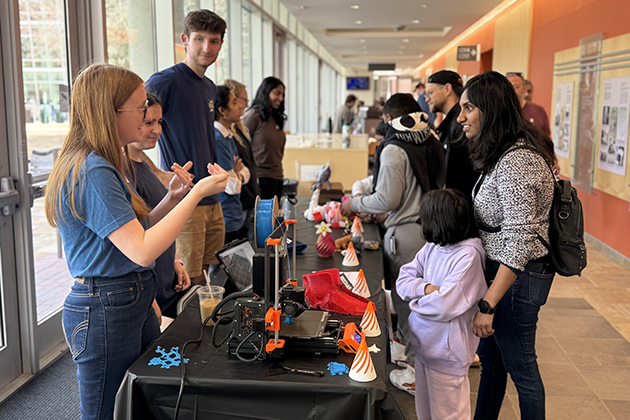 Several adults with their children learn about 3D printing from a group of graduate students