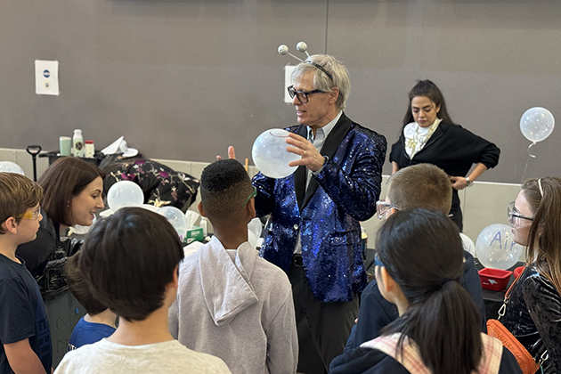 Man with a lot of balloons standing in a room full of elementary students