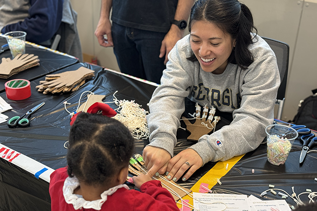 A little girl on one side of the table explores an anatomy demonstration while a female student on the other side of the table assists