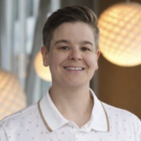 A woman with short brown hair wearing a white collared shirt smiles for a photo with hanging light fixtures in the background.
