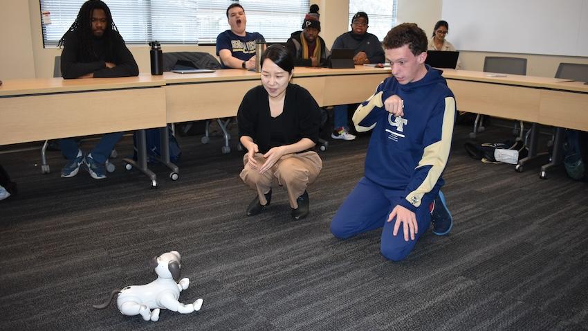 A robot dog sits in front of Assistant Professor Jennifer Kim and a student from the Georgia Tech Excel program.