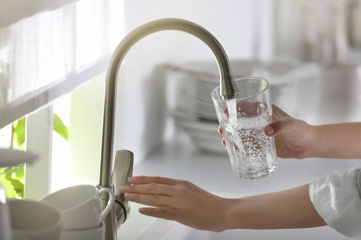 A woman's hands are shown filling a glass with water at a kitchen sink (stock image).