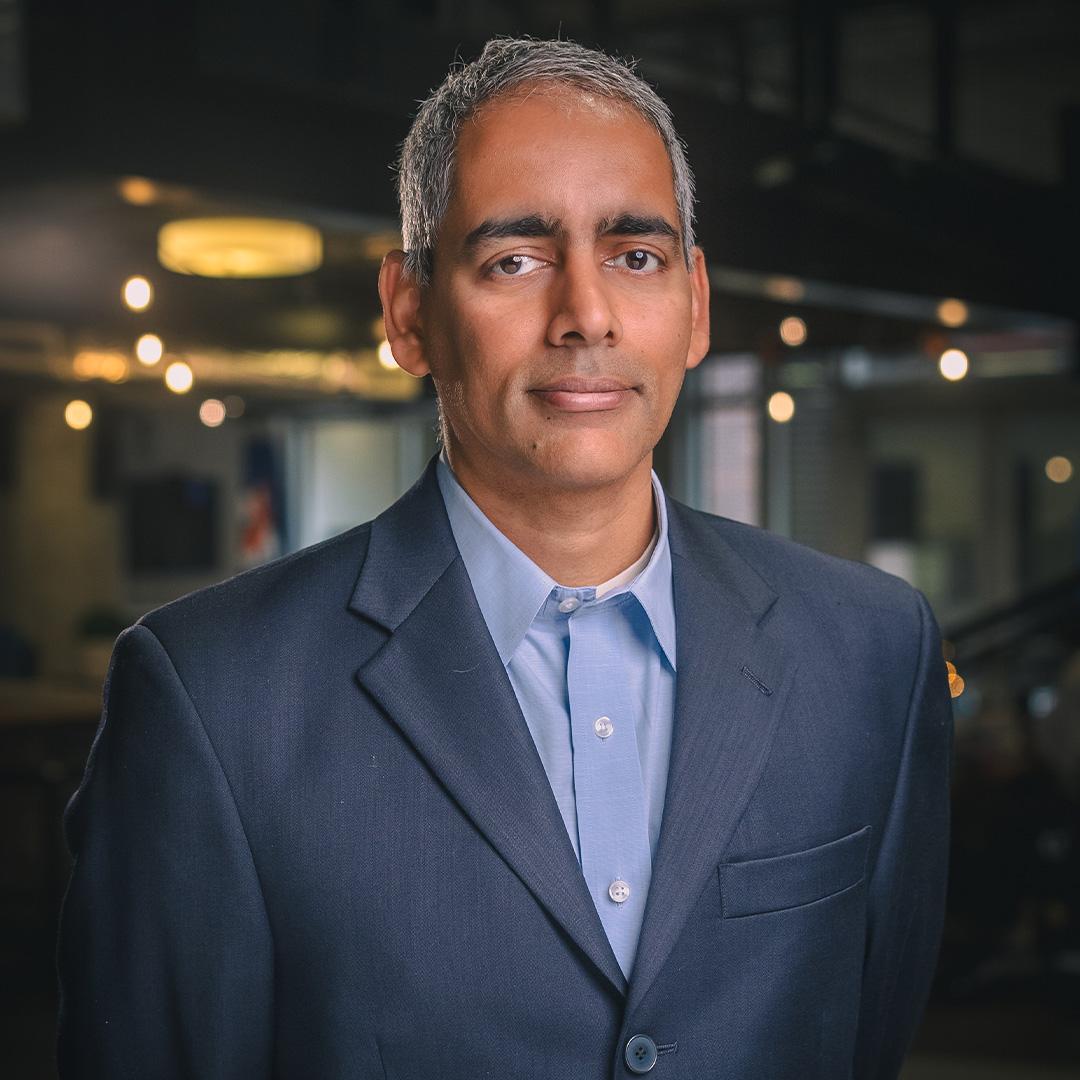 Karthik Ramachandran smiles in a navy suit coat