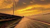 Amber-toned view of a solar farm with a windmill and clouds in the background.