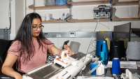 Female student operating a knitting machine in a research lab at Georgia Tech