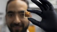 A male Georgia Tech researcher wearing a black glove holds a solar cell prototype.
