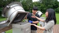A male and female researcher working with a metal piece of equipment outdoors with trees and grass in the background
