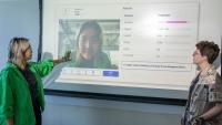 Xingyu Li and Alexandra Teixeira Riggs stand in front of a screen showing an emotion AI analysis of Li's facial expression.