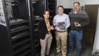 Three researchers stand in front of a rack of computing equipment.