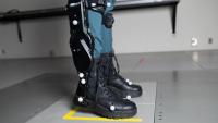 A person wearing black robotic exoskeleton boots standing on a gray platform.