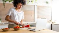 Woman chopping peppers in front of laptop