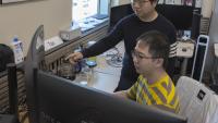 Assistant Professor Yalong Yang looks over the shoulder of Ph.D. student Tao Lu as they create a simulation of a news story presented in virtual reality.