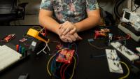 Josiah Hester sits at a desk in an electronics lab at Georgia Tech with an array of prototype projects and test equipment in front of him.