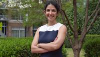 Farzaneh Najafi standing outside smiling with her arms crossed. Green foliage is visible in the background.