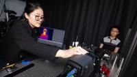 Dingding Han adjusts an infrared camera pointed at a test subject sitting in front of a black curtain. On a computer screen to her left is a thermal image of the subject. (Photo: Candler Hobbs)