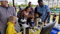 <p><em>A group looking through microscopes set up by GTRI volunteers at the Science Day in the Park (Photo Credit: Ethan Trewhitt). </em></p>