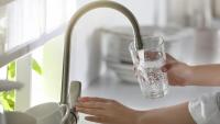 A woman's hands are shown filling a glass with water at a kitchen sink (stock image).