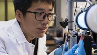 researcher with a white coat looking into a microscope