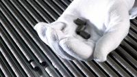 A white gloved hand holds 3 nuclear pellets with rows of nuclear pellets in the background